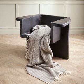 Modern black chair with a throw draped over it on a wooden floor.