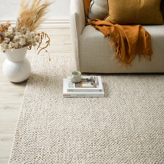 Beige rug with a vase of dried flowers, a book, and a blanket on a sofa in a living room.