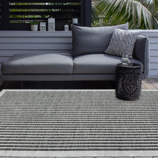 Gray outdoor sofa with cushions on a wooden deck, featuring a striped rug.