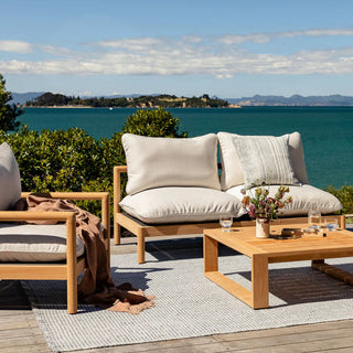 Outdoor furniture set with cushions and a coffee table by a scenic waterfront.
