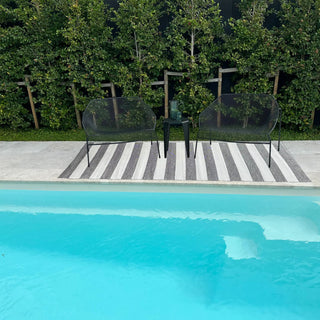 Two black chairs on a striped rug by a pool with greenery in the background