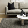 Gray sofa with a black pillow and a marble coffee table in a living room setting.