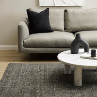 Gray sofa with a black pillow and a marble coffee table in a living room setting.