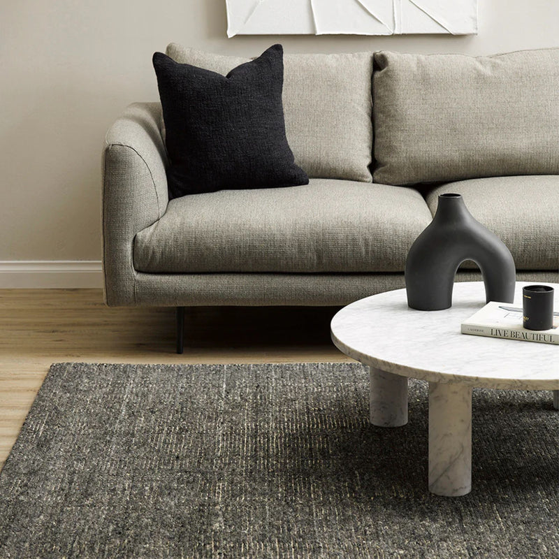 Gray sofa with a black pillow and a marble coffee table in a living room setting.