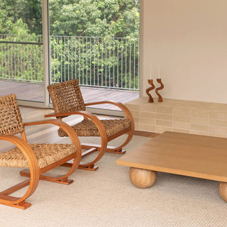 Two wicker chairs and a wooden coffee table in a room with a view of greenery outside.