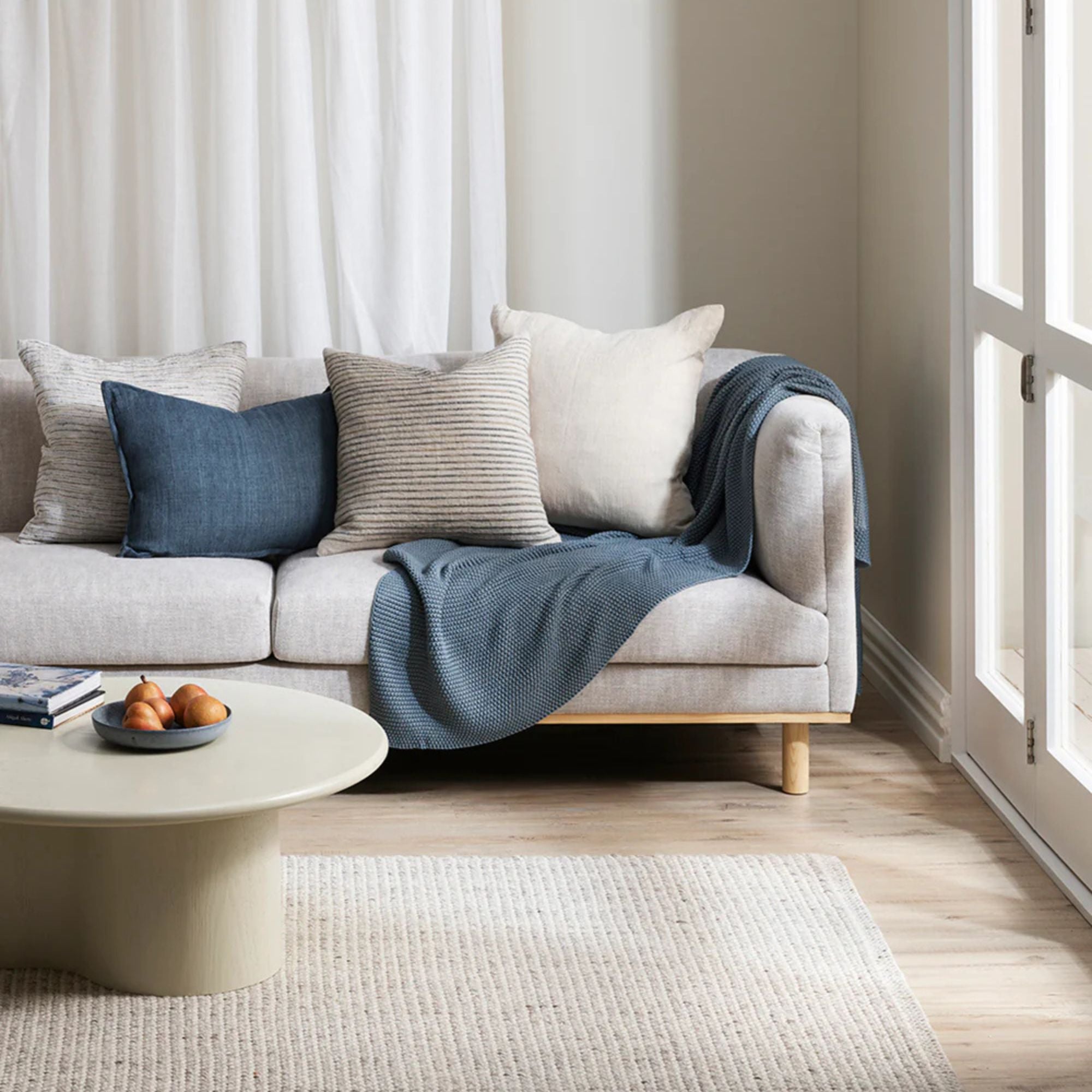 Light gray sofa with blue throw blanket and pillows in a bright living room.