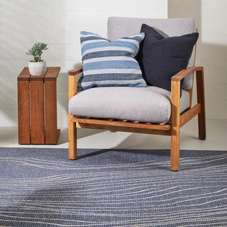 Chair with wooden frame and gray cushion, featuring blue and black striped pillows, next to a wooden side table with a plant.