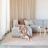 Light gray sofa with a plaid blanket in a living room setting with beige curtains and rug.