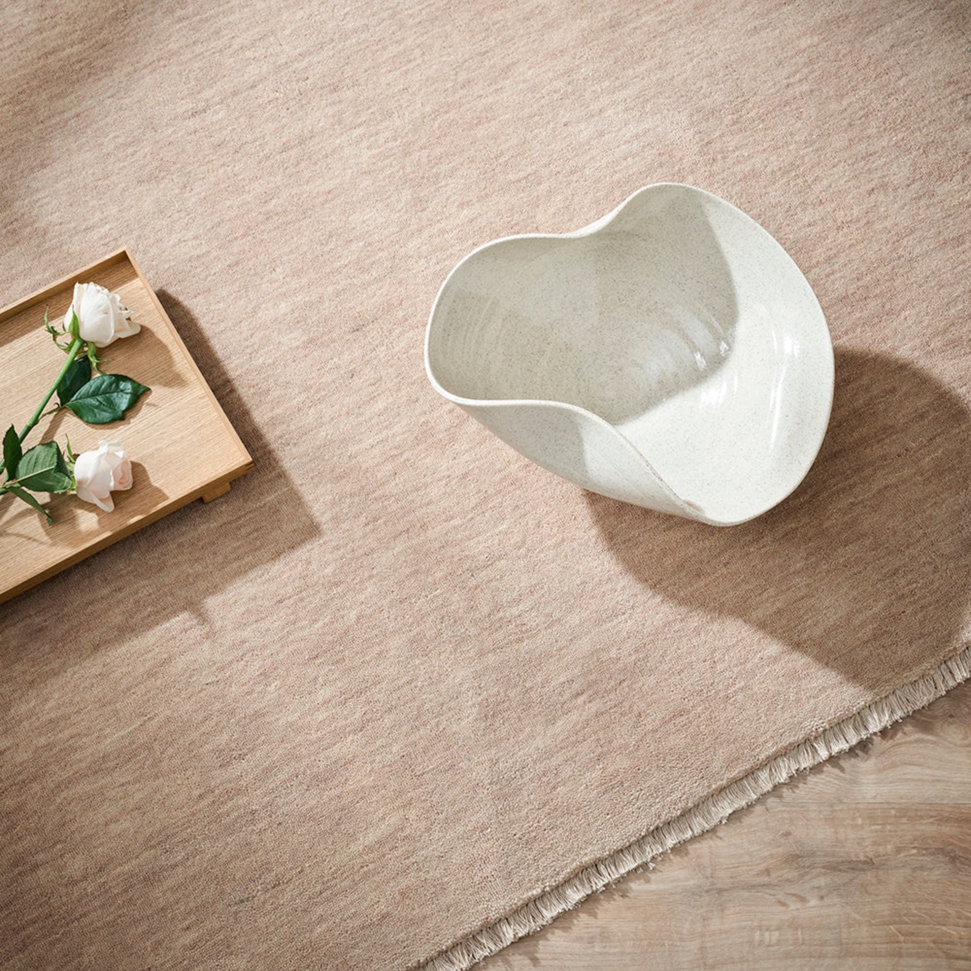 White ceramic pitcher on a beige rug with a wooden tray and flowers.