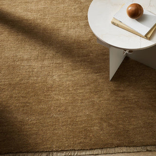 Brown rug with a white side table and books in the corner