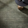 Textured green carpet with a black side table and a round object on a wooden surface.
