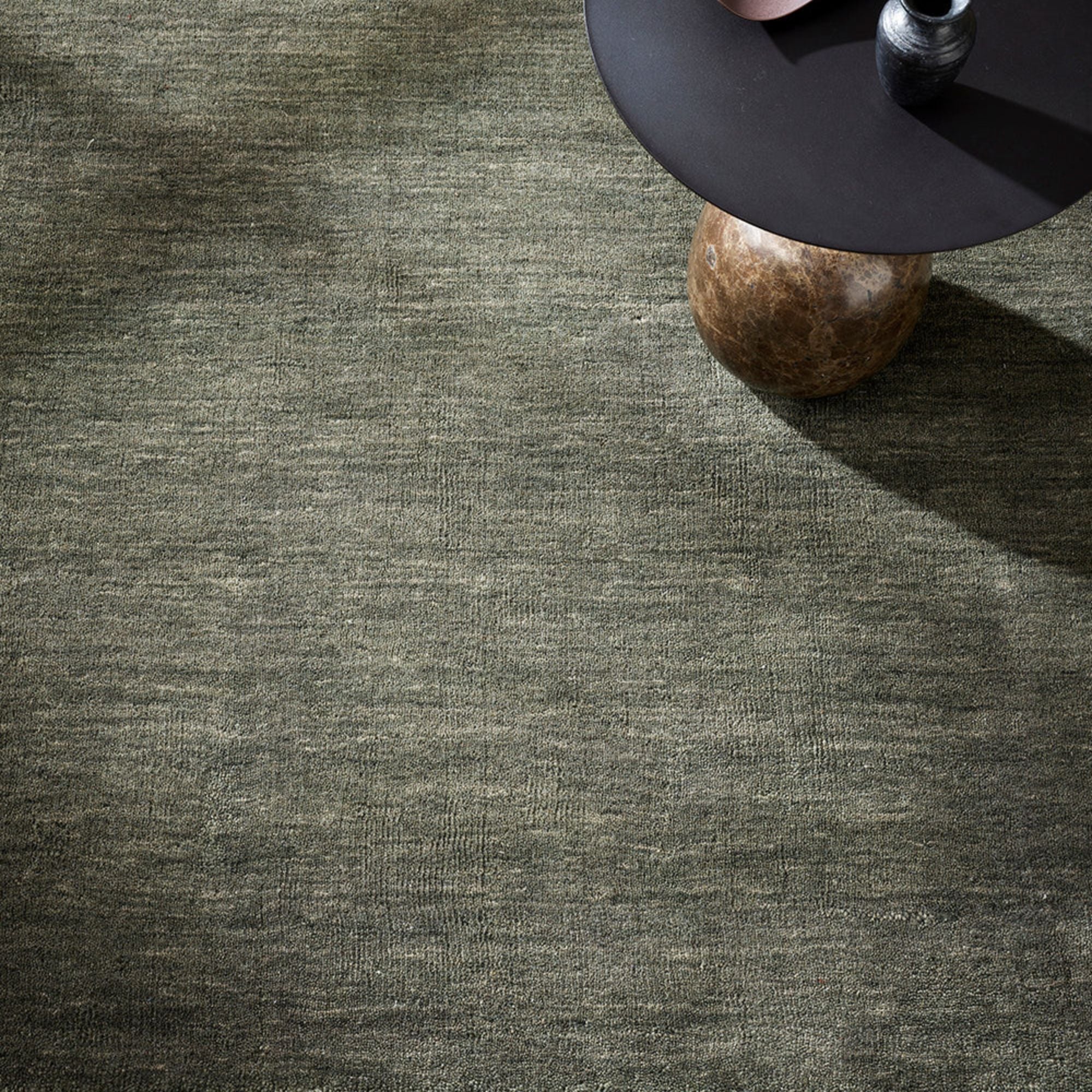 Textured green carpet with a black side table and a round object on a wooden surface.