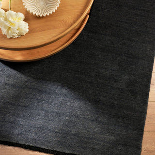 Dark gray rug with a wooden tray and white flowers on a wooden floor.