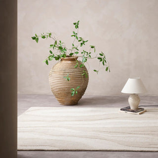 Decorative vase with greenery on a wooden table against a beige wall.
