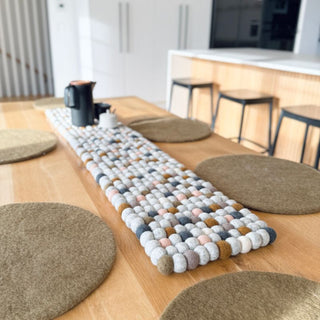 Neutral felt ball table runner styled on a wooden dining table with round placemats