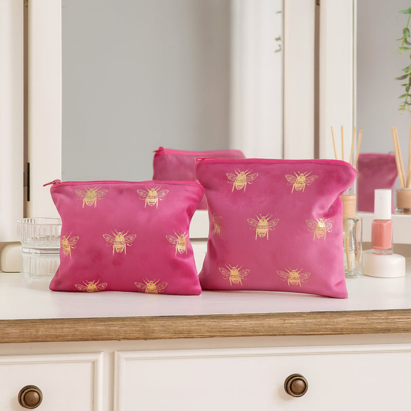 Two pink pouches with bee patterns on a vanity counter.