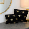 Black toiletry bags with bee patterns on a gray surface, with a mirror and lamp in the background.