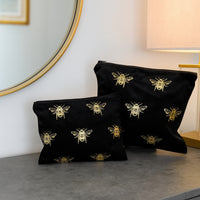 Black toiletry bags with bee patterns on a gray surface, with a mirror and lamp in the background.