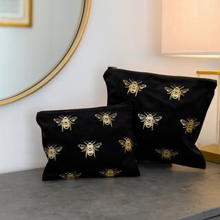 Black toiletry bags with bee patterns on a gray surface, with a mirror and lamp in the background.