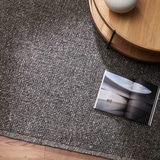 Gray textured rug with a wooden side table and a book on a dark surface