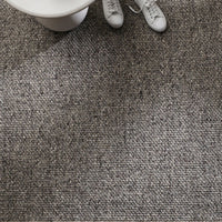 Close-up of a textured gray carpet with white shoes and a white object in the corner.