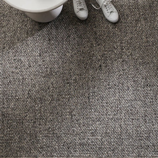 Close-up of a textured gray carpet with white shoes and a white object in the corner.